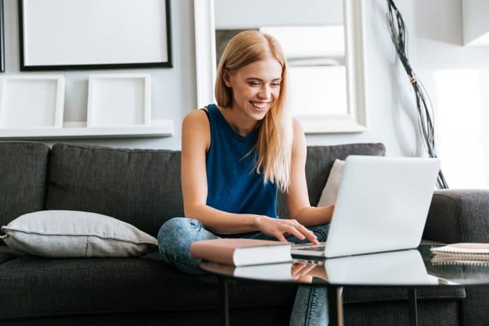 Happy woman sitting on sofa and using laptop at home mulher no celular